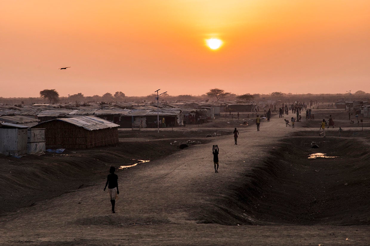Individuals walking a road through a refugee camp at sunset.