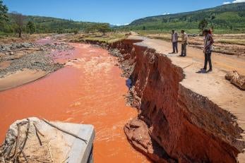 Three prosper global employees next to a clay colored river impacted by flooding