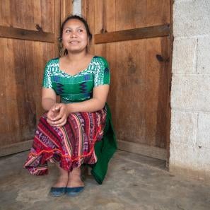 Young woman sitting in corner of room, in front of two doors.