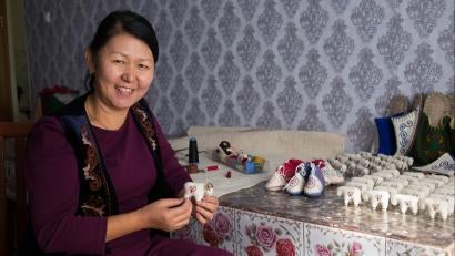 Woman in kyrgyzstan holding a felted ram and looking at the camera