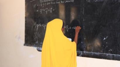 Somalian woman at chalkboard working on a math problem.