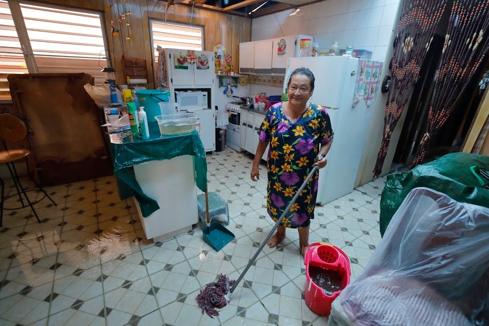 Carmen stands in her kitchen with a mop and bucket