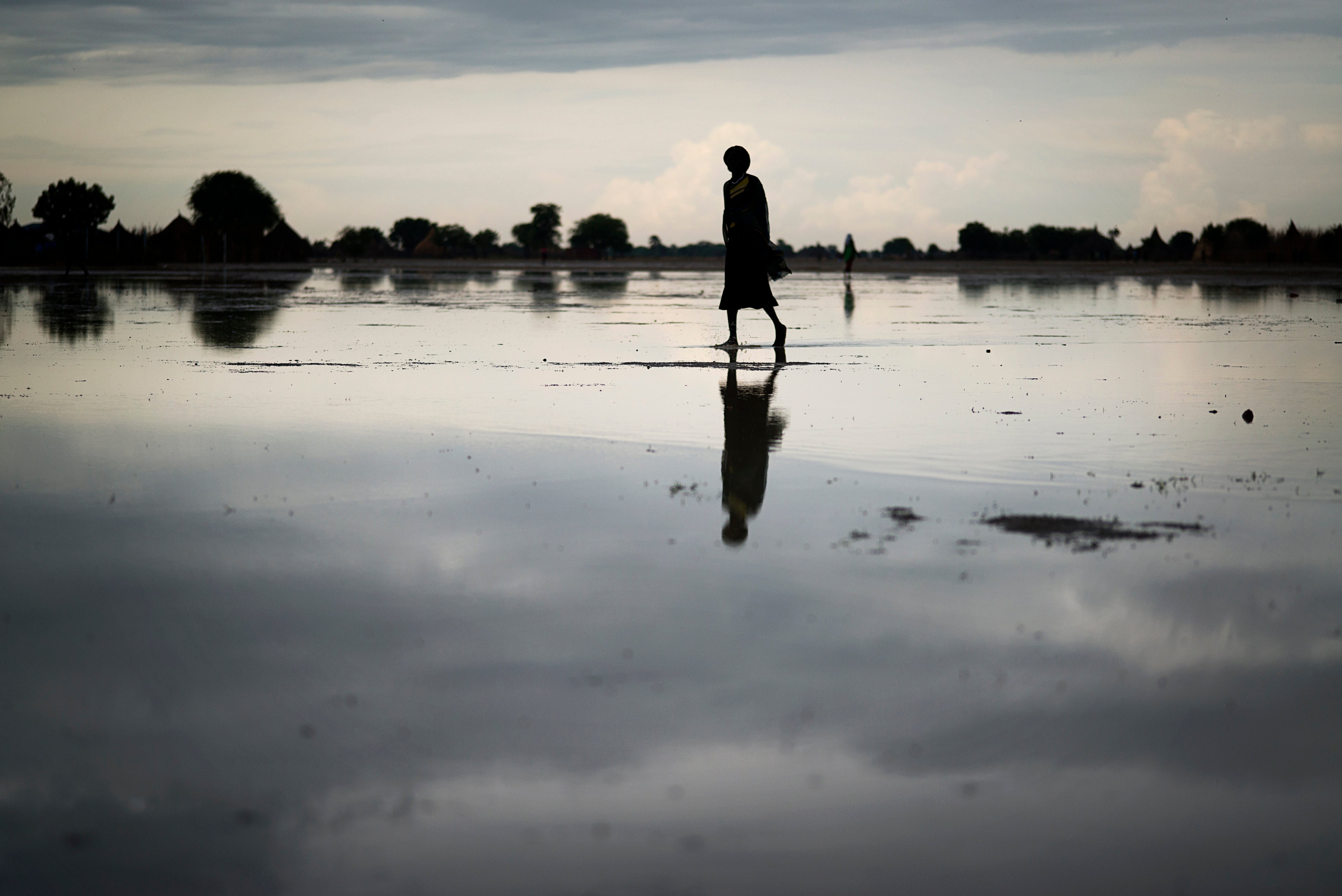 Woman walking under cloudy sky with silhouette reflected on wet ground
