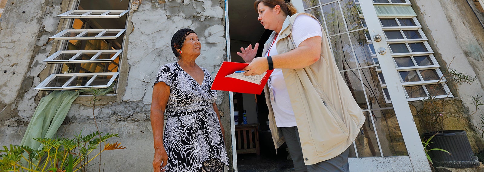A Prosper Global team member holding a folder, paper and pen speaks to a woman in Puerto Rico
