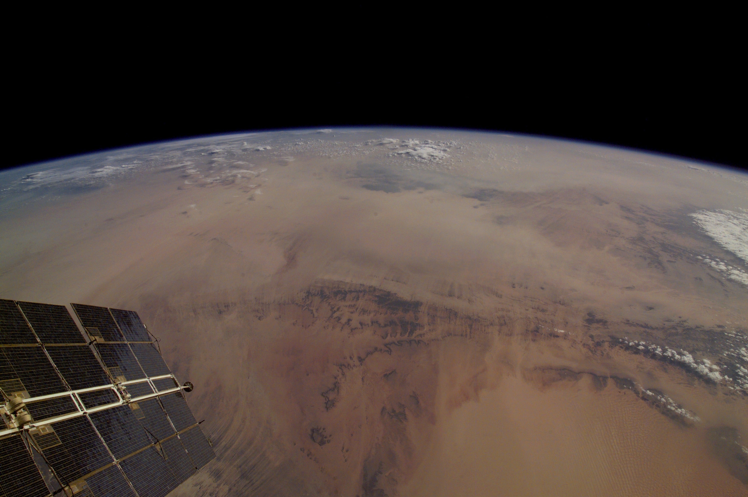 A photo showing a portion of a satellite and the curve of the earth, with the brown Sahara making up the majority of the land shown