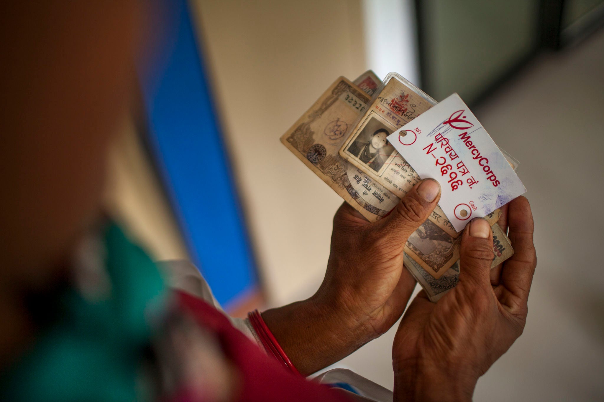 Image: Hands holding cash and a Prosper Global ID card during a distribution of emergency cash