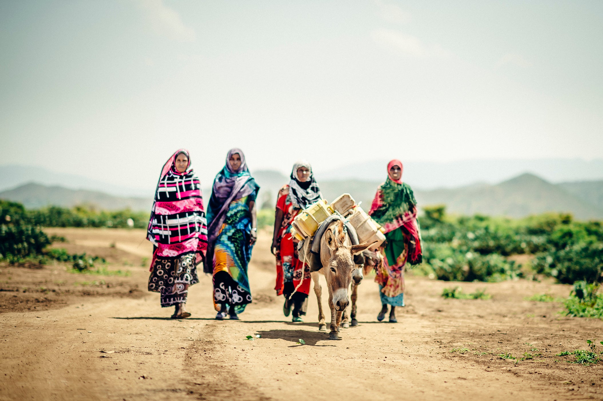 Four women in Ethiopia wearing bright colors and walking behind a donkey