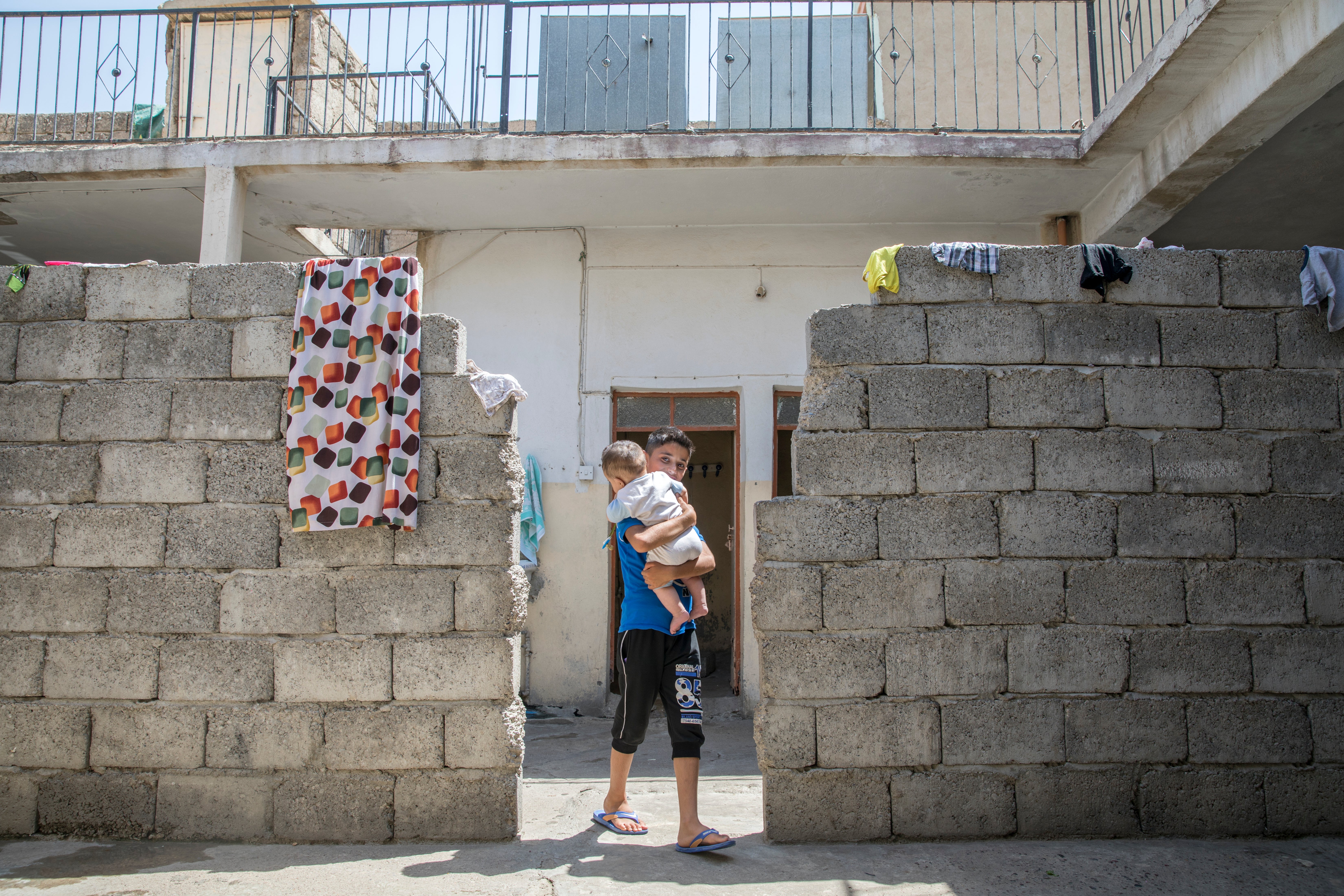 A boy in a cinderblock doorway holding a baby