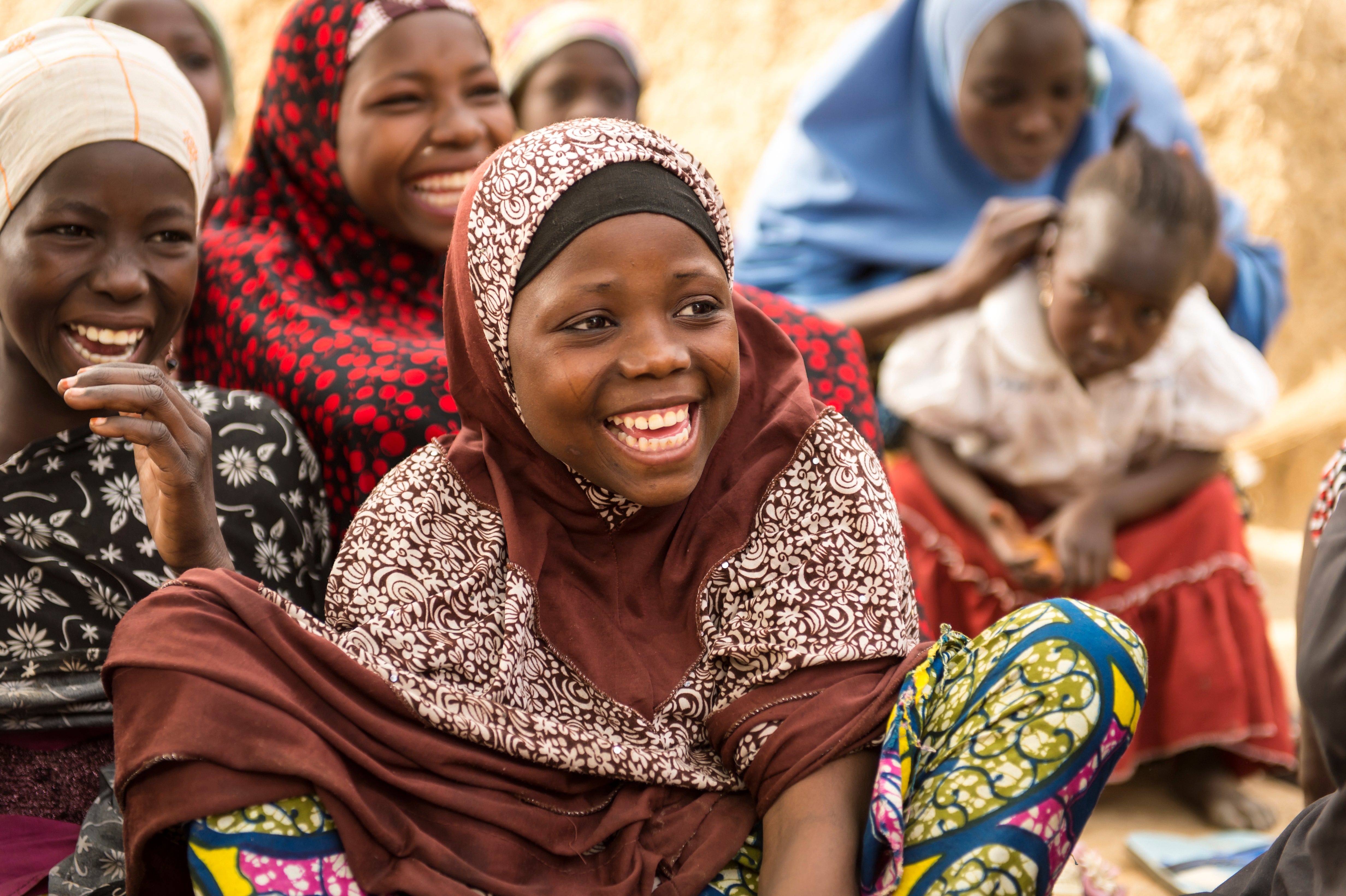 A girl sitting on the ground with other girls nearby, all laughing, in Nigeria