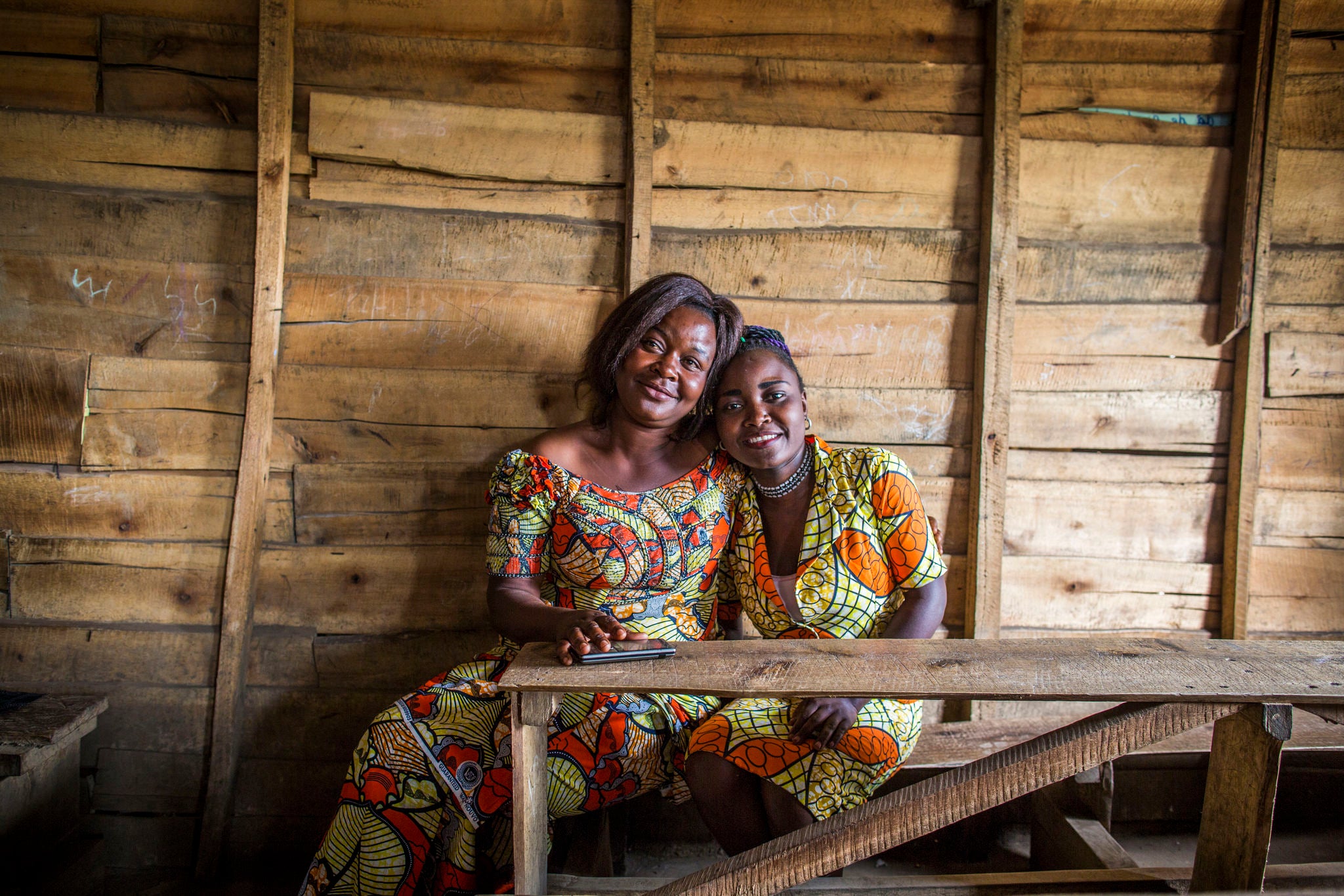 A mother and daughter sit together on a wood bench.