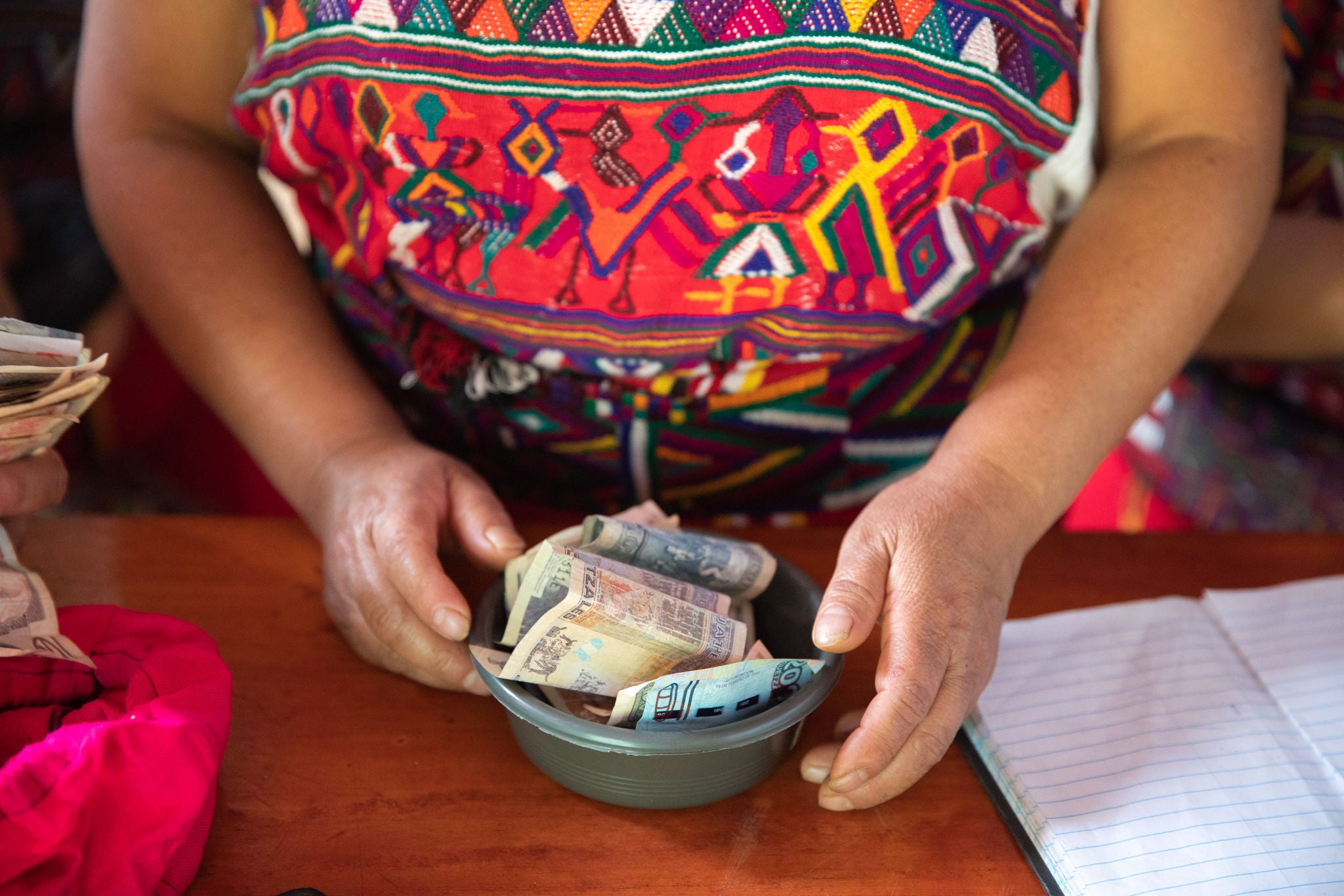 The hands of a savings and loan group grasp a bowl of paper money in Acul, Guatemala.