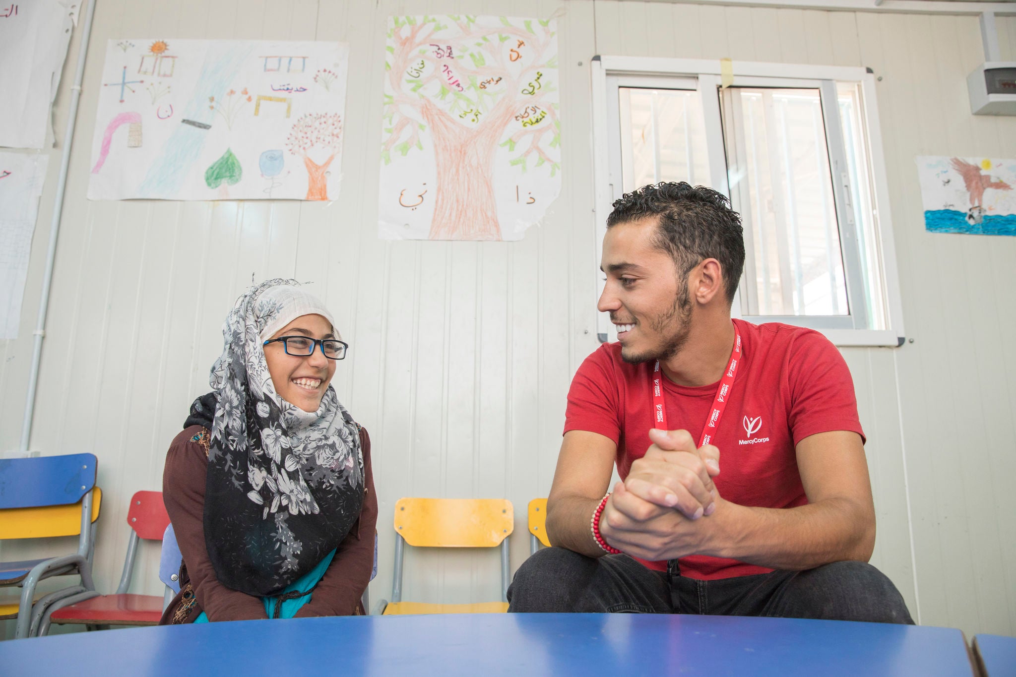 A Prosper Global staff member sits at a table smiling with a young participant in Azraq, Jordan.