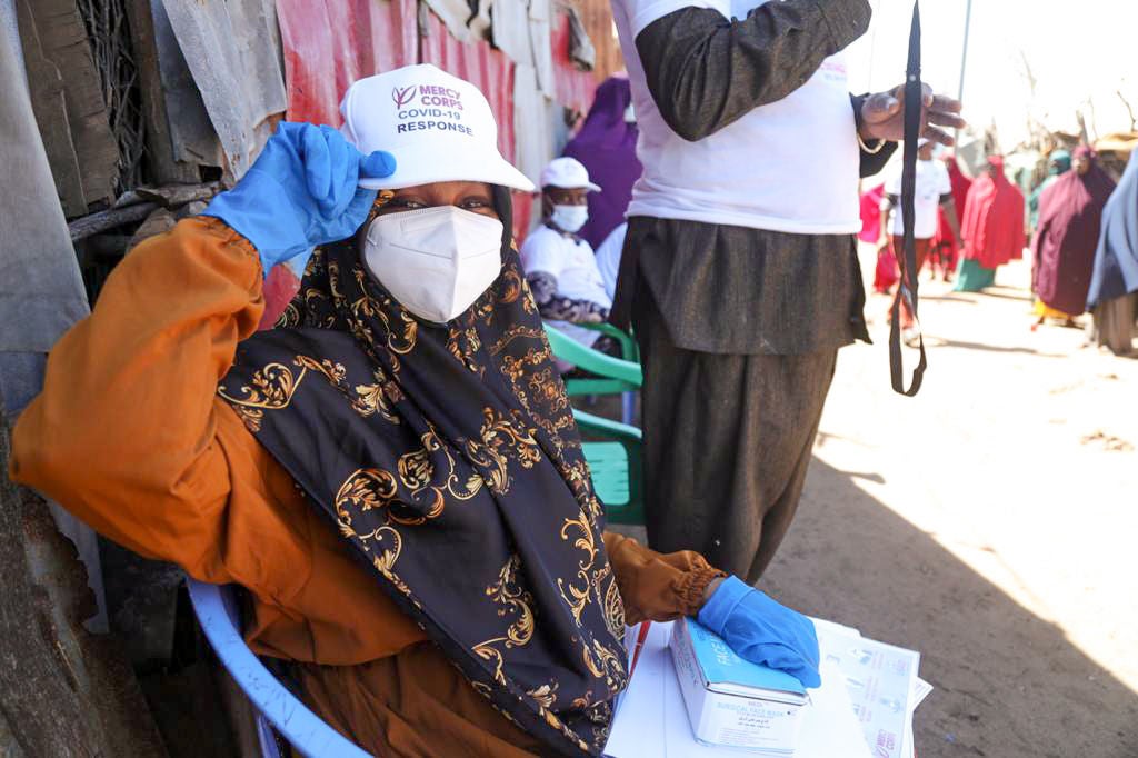 A person wearing face mask shows off their Prosper Global hat to the camera on a busy street in Somalia.