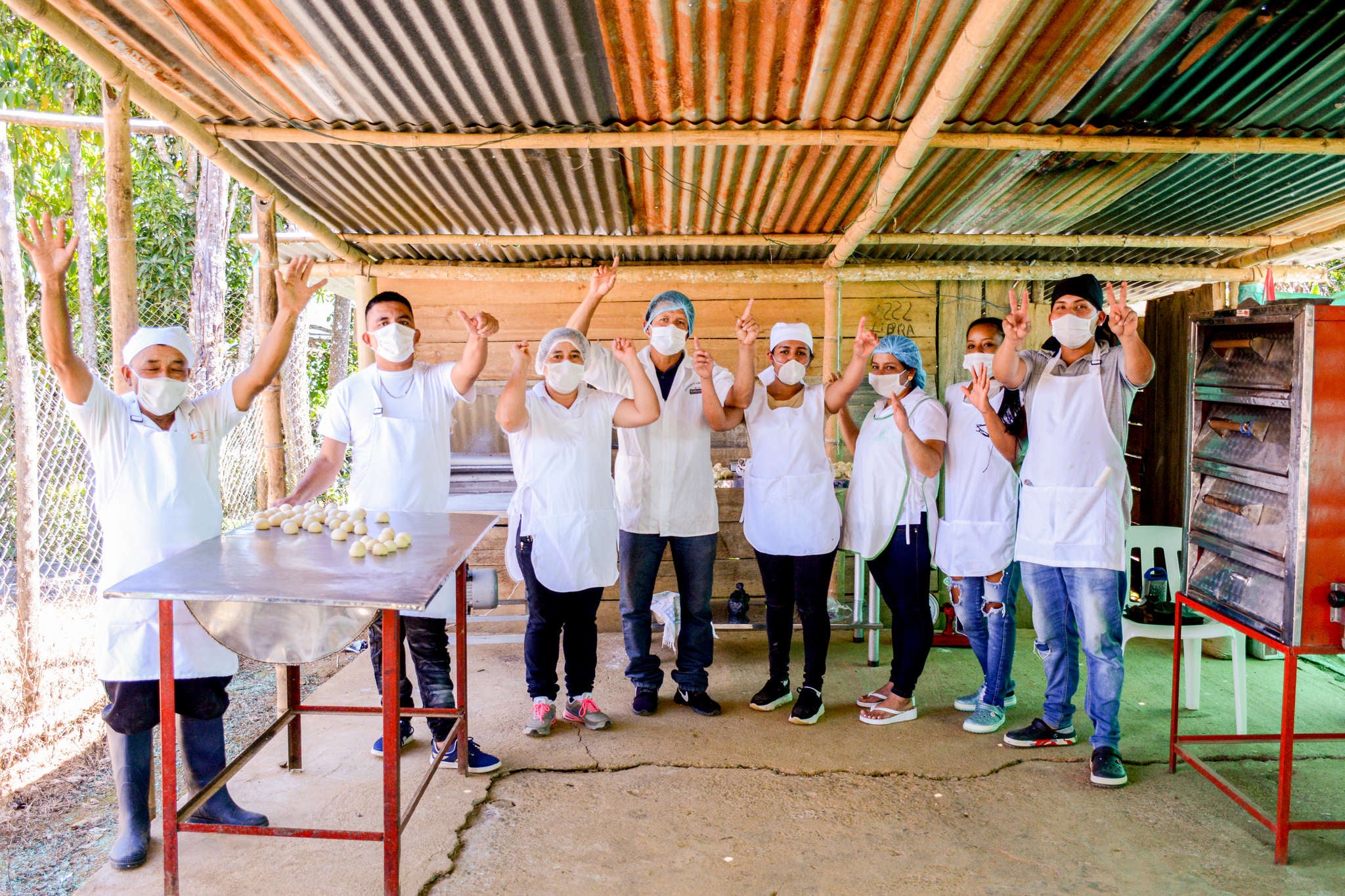 A group of bakers wave at the camera from an outdoor kitchen.