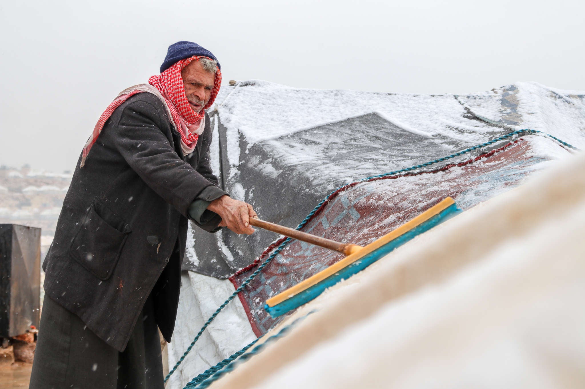 A person uses a broom to try and clear the snow away from their damaged tent.
