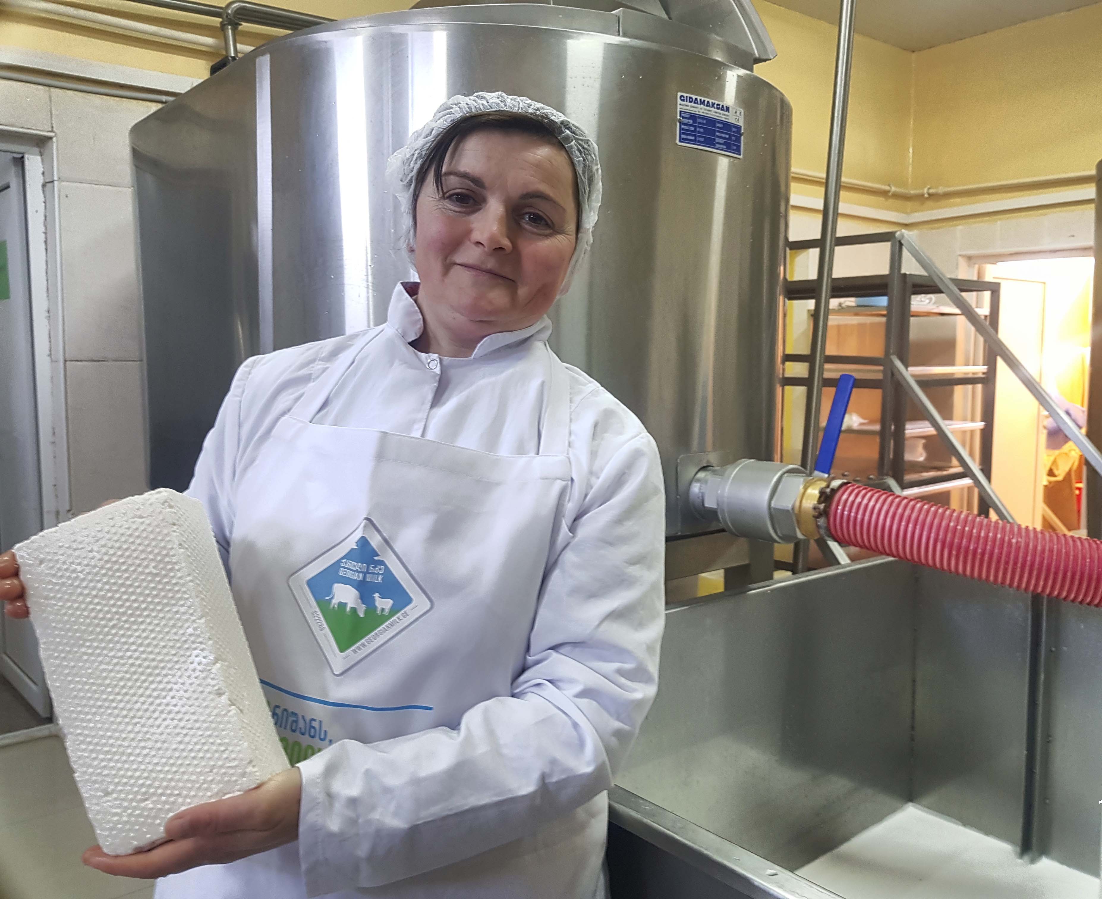 A person holds a cheese block in a cheese making facility.