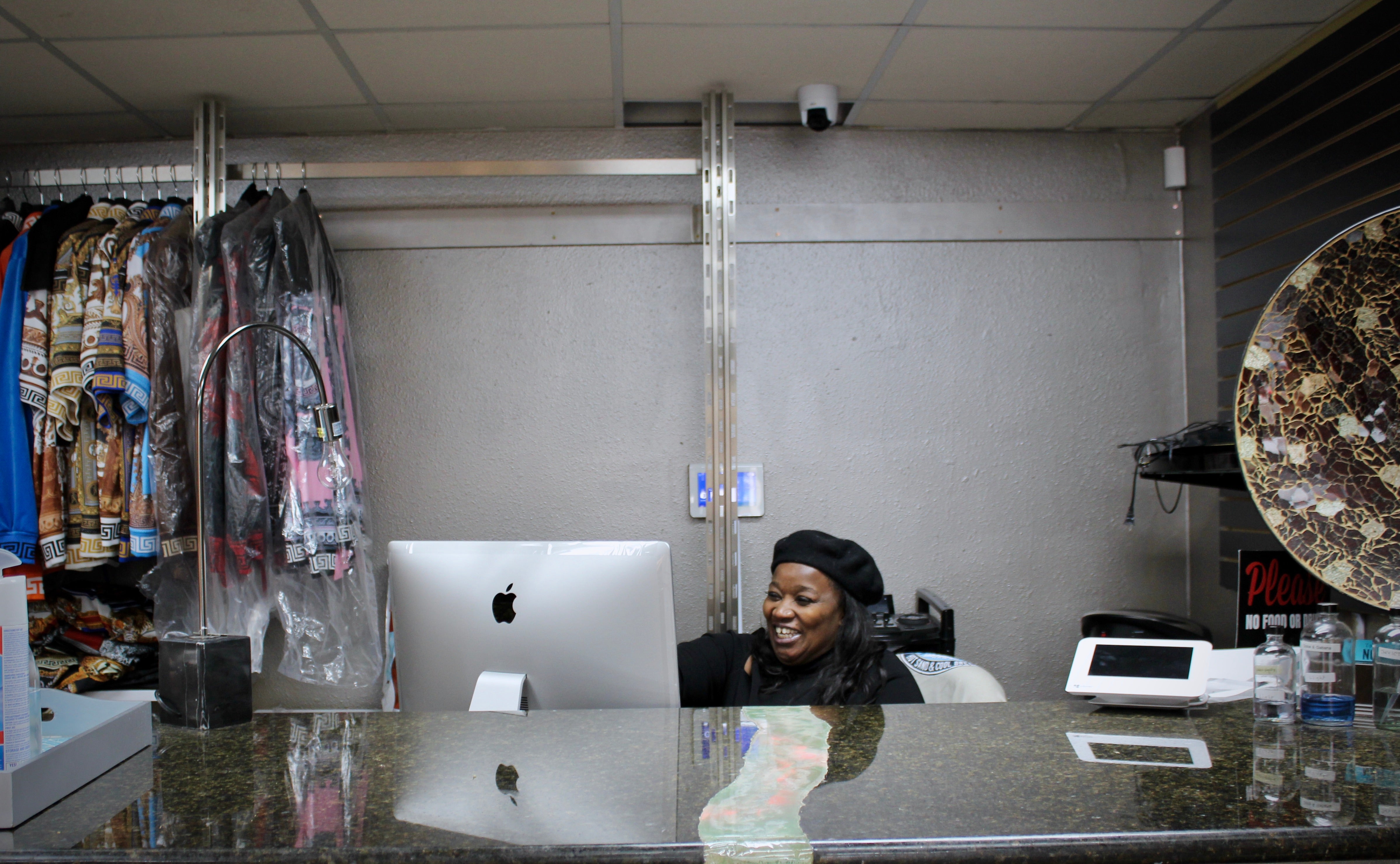 a black woman entrepreneur dressed in black sits behind her store counter with a smile