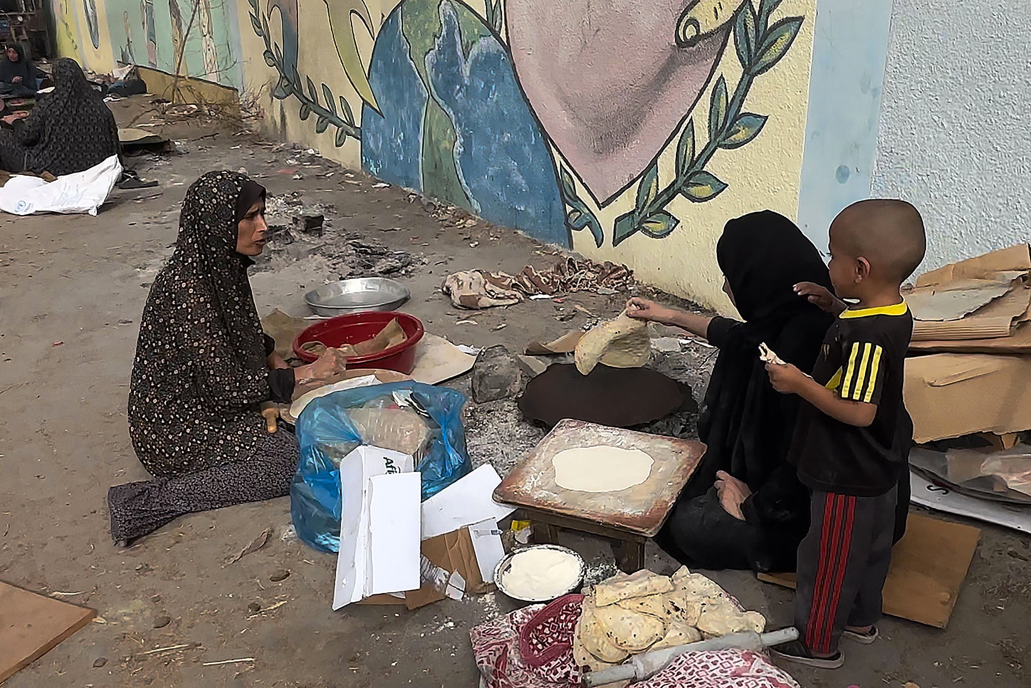Two women in Gaza prepare flatbread while a child looks on