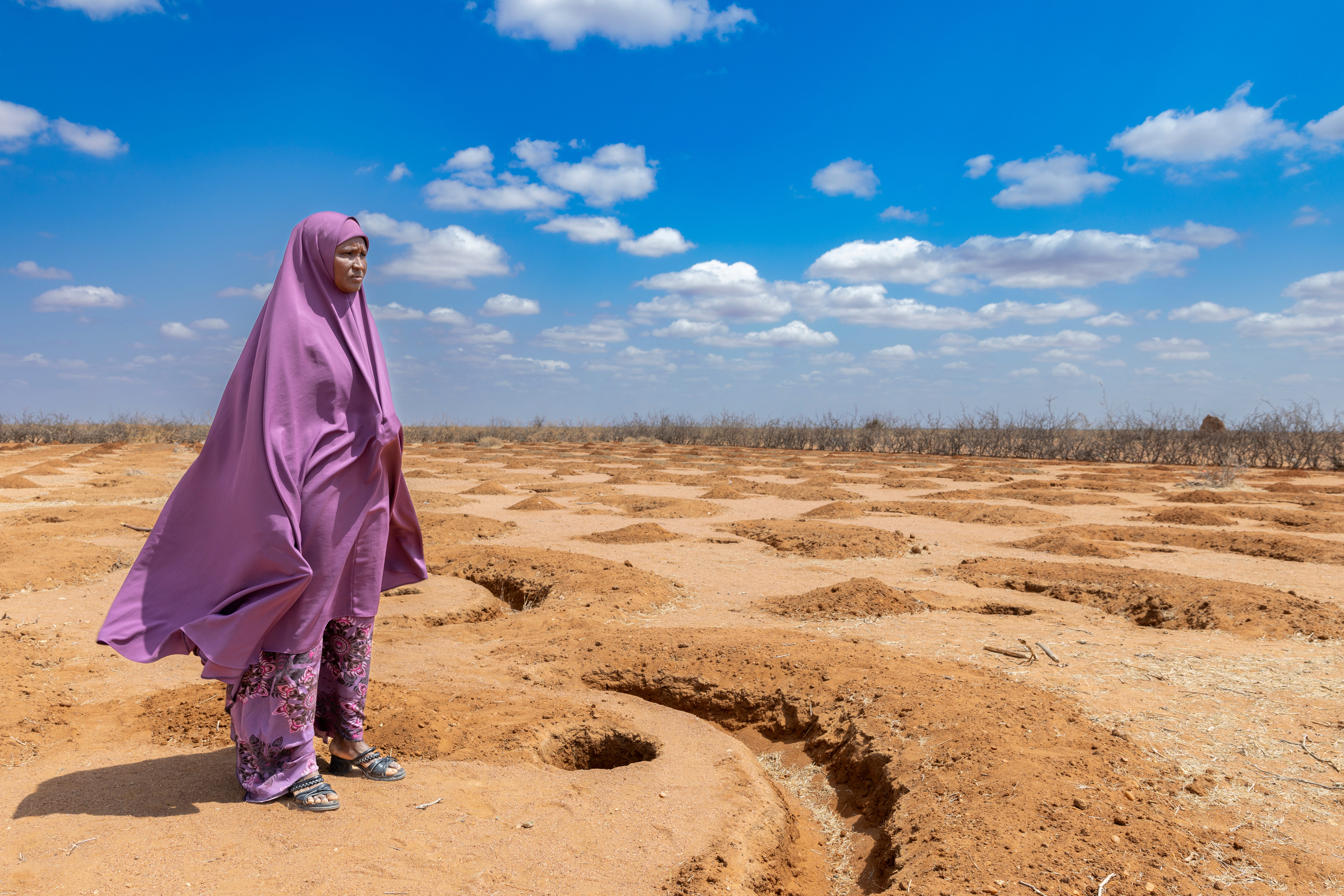 Kenyan woman looks out over arid agricultural land.