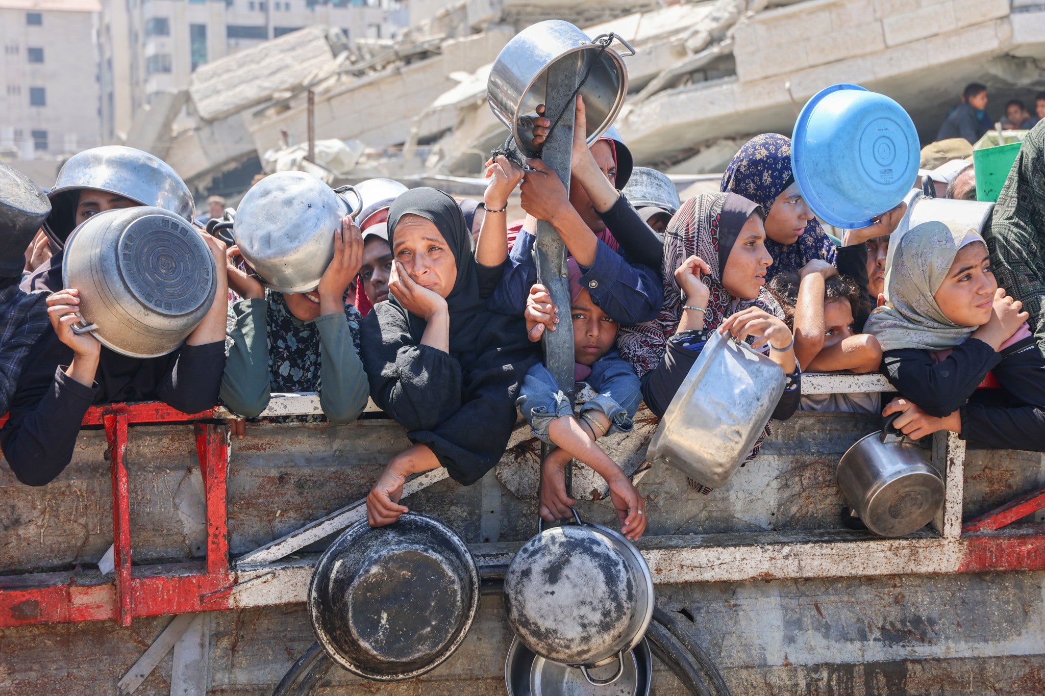 Palestinians holding empty pots and pans await a food delivery