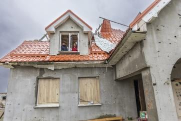 Ukrainian mother and father stand in window of damaged home.
