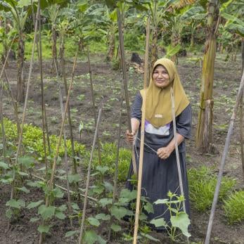 Indonesian woman in field with with hand tool, smiling.