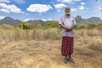 Kenyan man stands in rangeland with mountains in background.