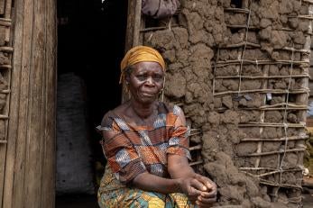 A woman poses outside a mud building in the democratic republic of congo