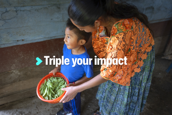 A child holds a basket of vegetables while a woman stands behind him
