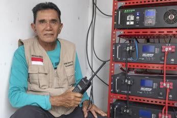 Indonesian man with hand radio and broadcasting equipment intended for use during emergency moments.