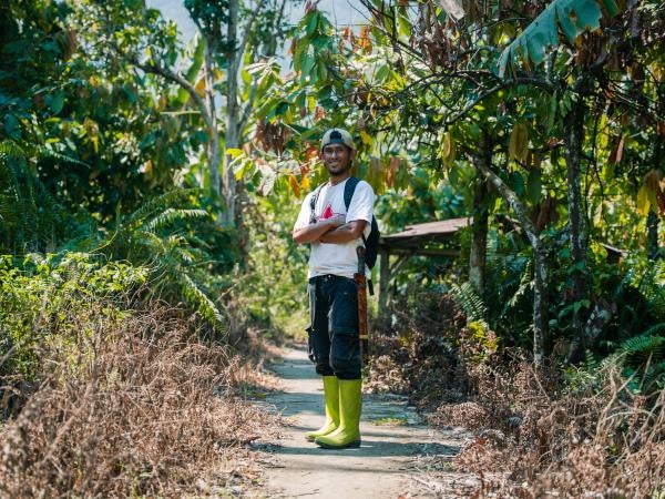 Marwan stands among cocoa trees on his farm in Indonesia.