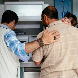 Prosper global team member helping a father (holding his daughter) to use an atm