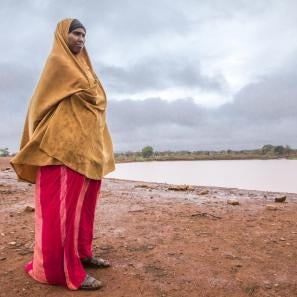 Woman dressed in dark yellow and red, standing near a body of water