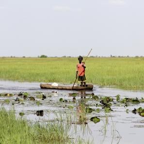 Person navigating a small wooden canoe in shallow water