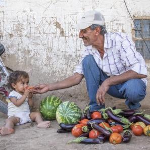 Man and baby with vegetables and fruit on the ground between them
