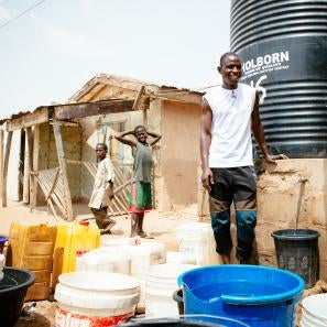 Nigerian man in front of water cistern and home.