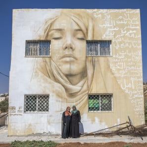Two woman in front of a building with a large mural painted on it.