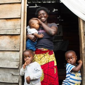 Justine stands in the doorway of her small wooden home, which is the only source of light for the tiny space built on lava rock. she and her family are grateful for the prosper global tap stand across the street that brings clean water close to their home. photo: liz hummer/prosper global