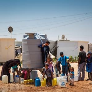 Families get water from a tank at a refugee camp