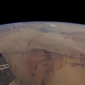 A photo showing a portion of a satellite and the curve of the earth, with the brown sahara making up the majority of the land shown