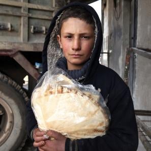 A boy wearing a black hooded sweatshirt holds bread in syria