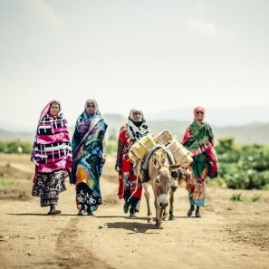 Four women in ethiopia wearing bright colors and walking behind a donkey
