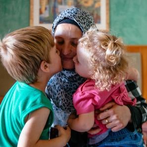 A woman receives kisses on her cheeks from a young boy and girl as she holds them tight