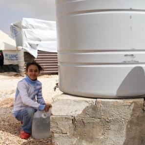A girl and boy next to a large white water tank at a refugee camp in jordan