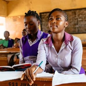 A high school student in nigeria leans forward in their seat inside a classroom with students. 