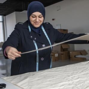 Jordanian woman measures textiles in workspace.