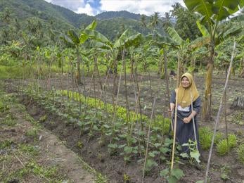 Indonesian woman in field with with hand tool, smiling.